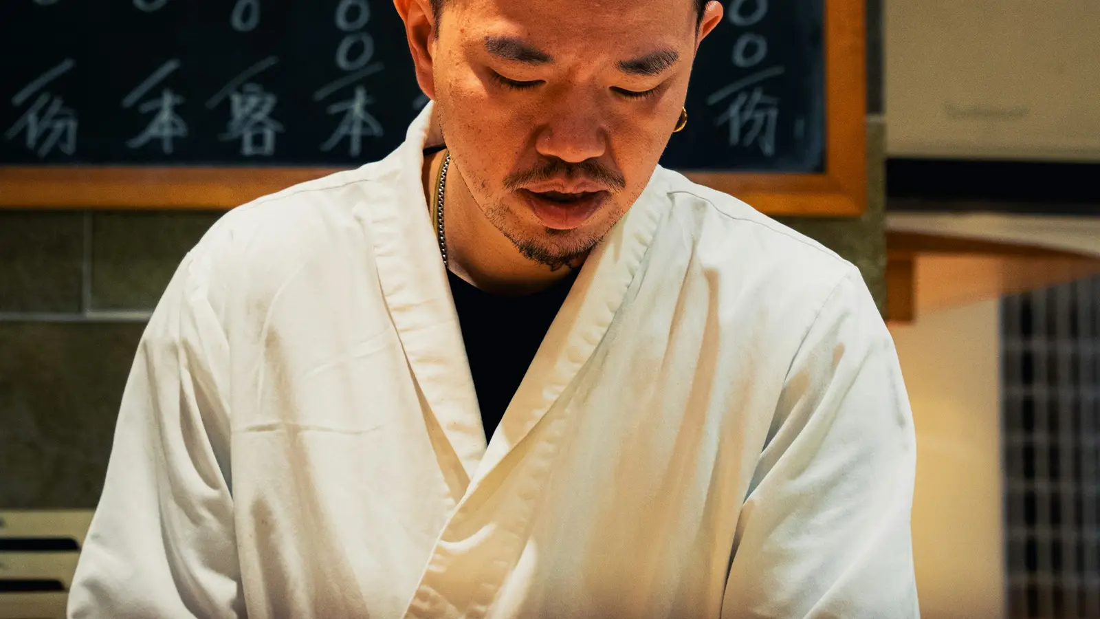 A sushi chef at work in front of a handwritten blackboard menu